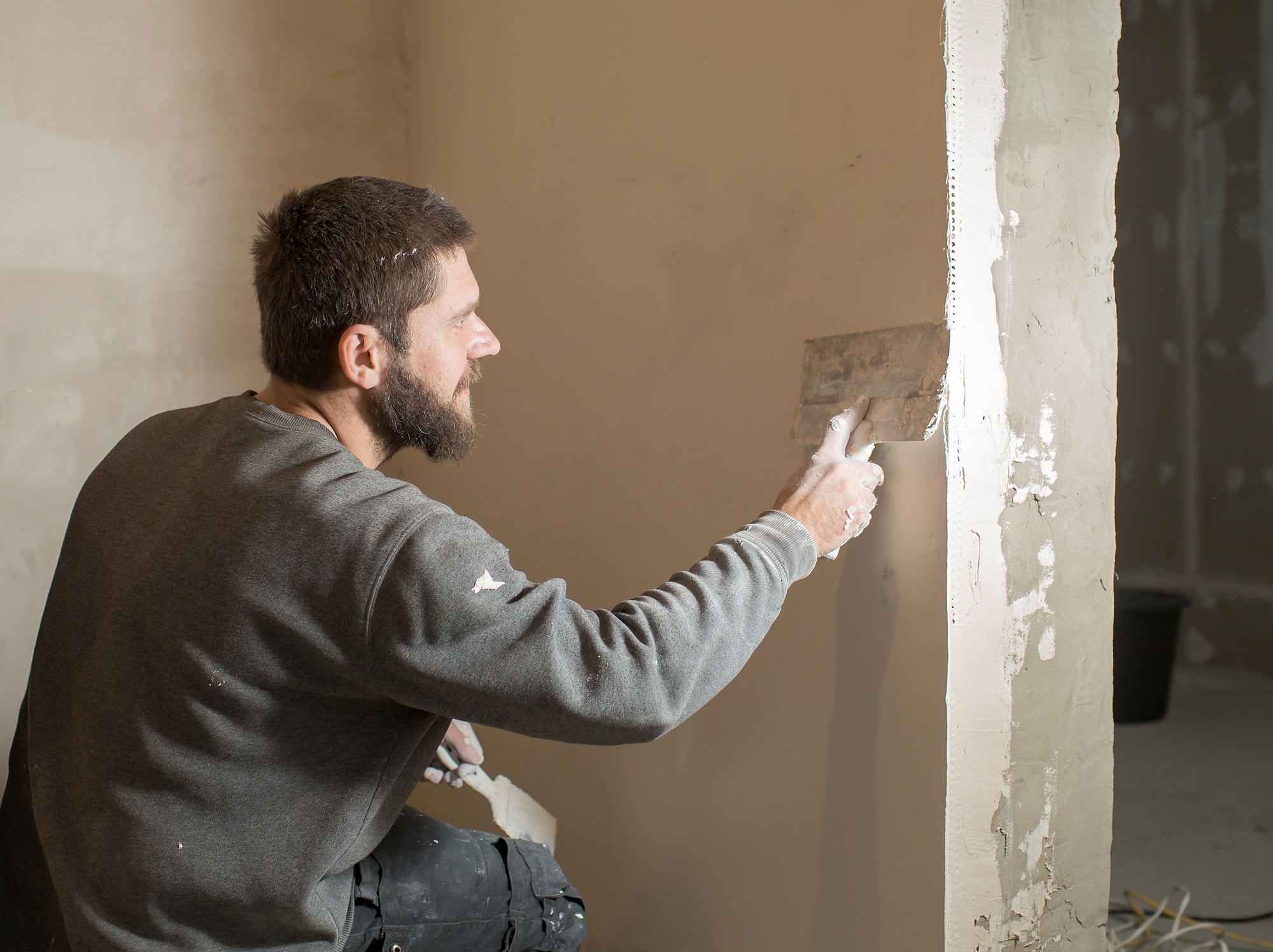 a male plasterer plasters a concrete wall with a spatula.